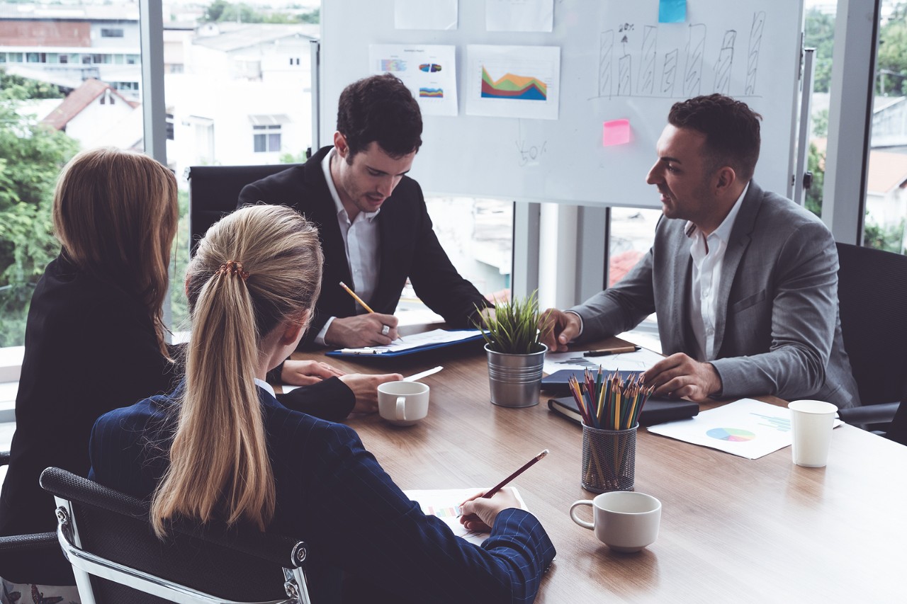 Businessman executive in group meeting discussion with other businessmen and businesswomen in modern office with coffee cups and documents on table. People corporate business working team concept.