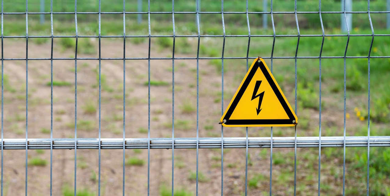 High voltage dangerous electric sign on fence. Warning sign, yellow triangle with lightning on a fence made of metal mesh.