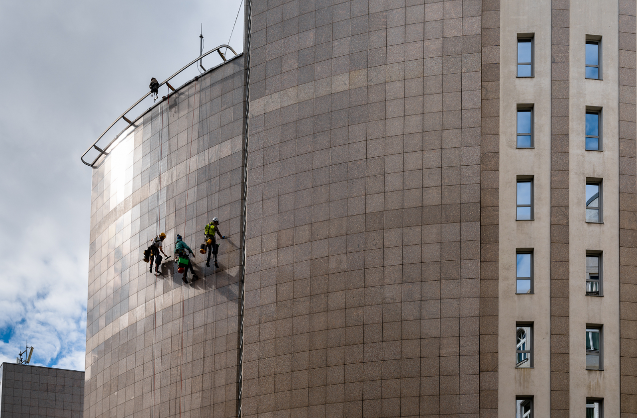 Budapest, Hungary - 4 October, 2022: rope access technicians hanging on the side of a metal high-rise building and cleaning the facade